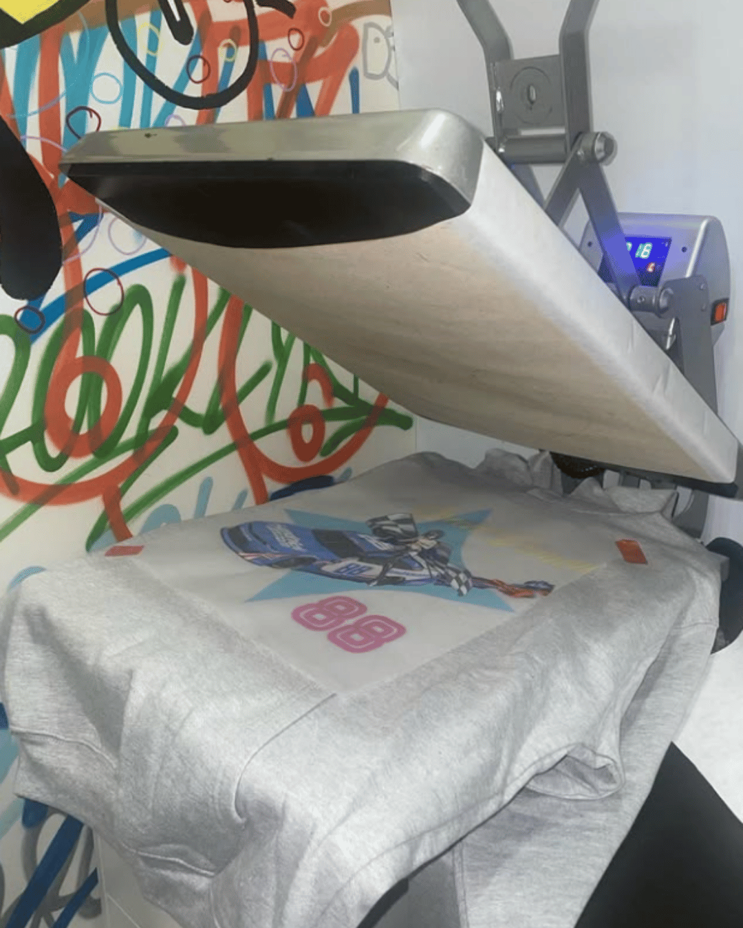 Heat press machine printing a graphic design onto a gray T-shirt in the Remix'd Prints apparel studio.