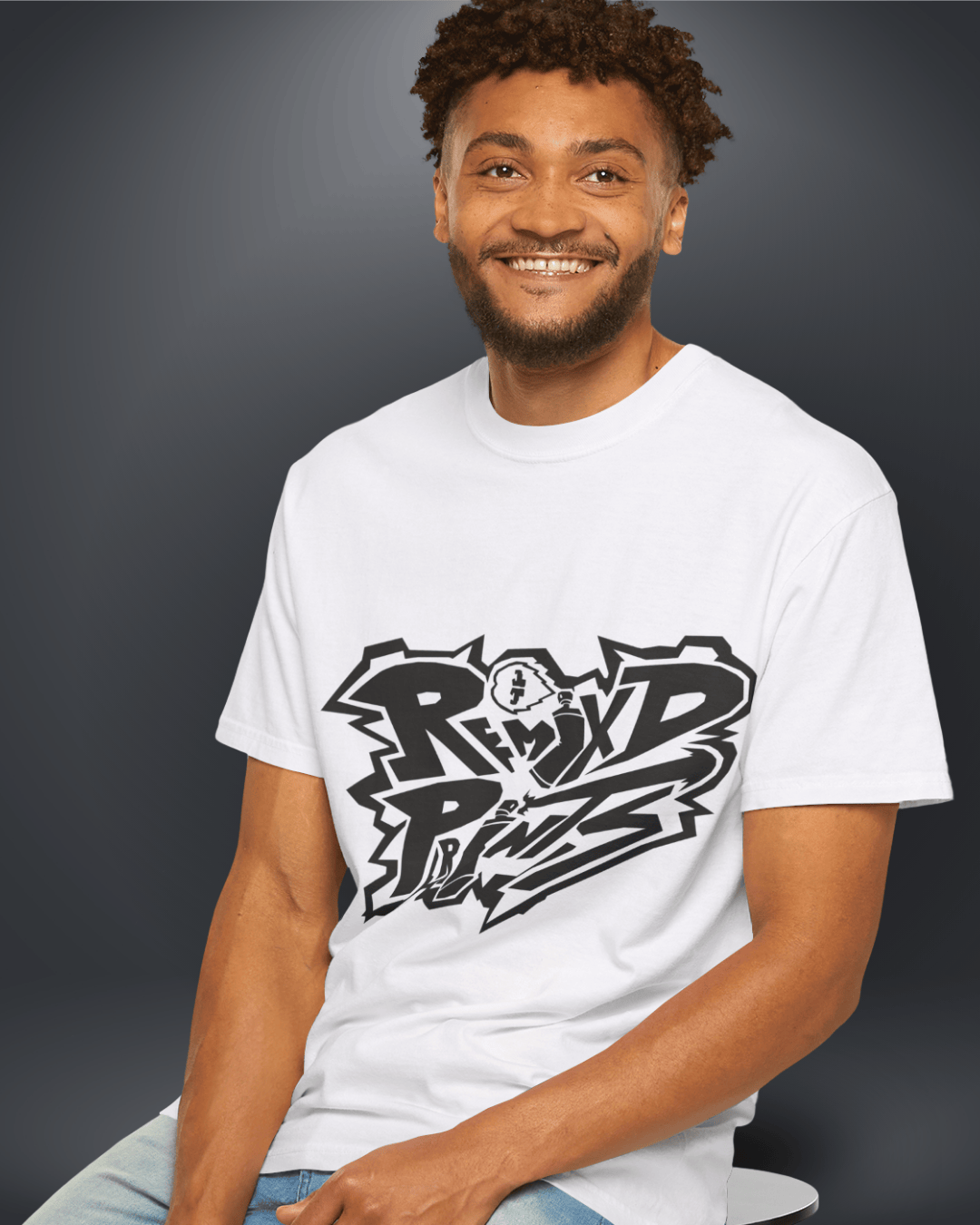 Smiling man wearing a white Remix’d Prints T-shirt featuring a bold black graffiti-style logo against a dark studio background.