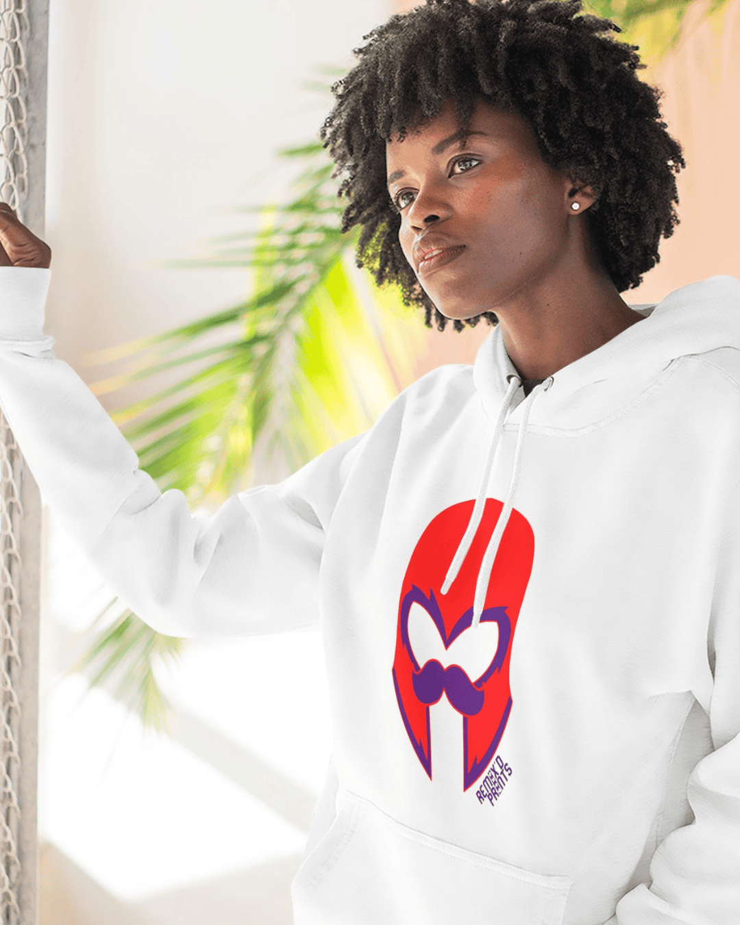 Woman wearing a white hoodie featuring a bold red IFC graphic design, standing near a window with natural light and greenery in the background.